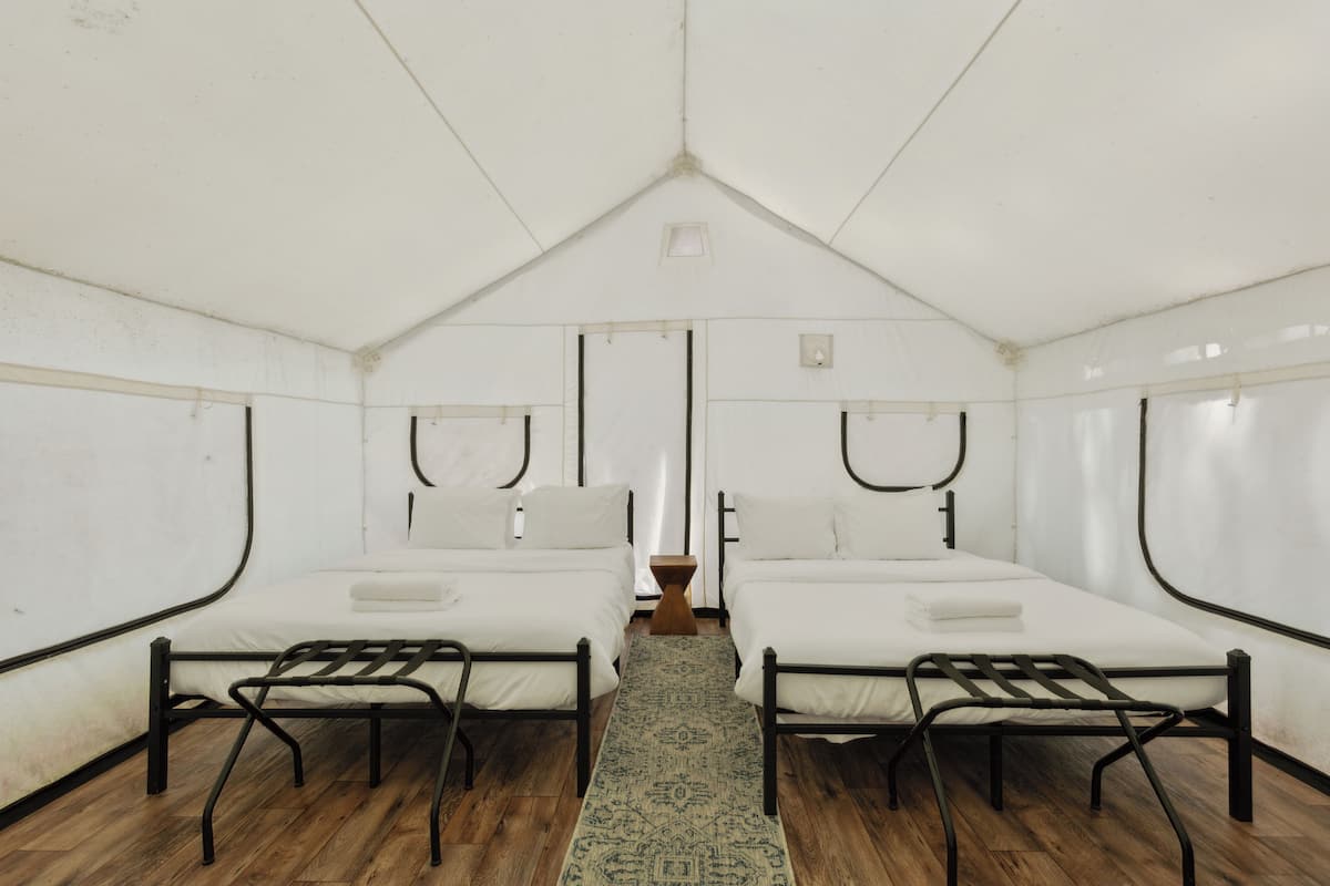 A tented room with two beds, a wooden floor, and a central rug.