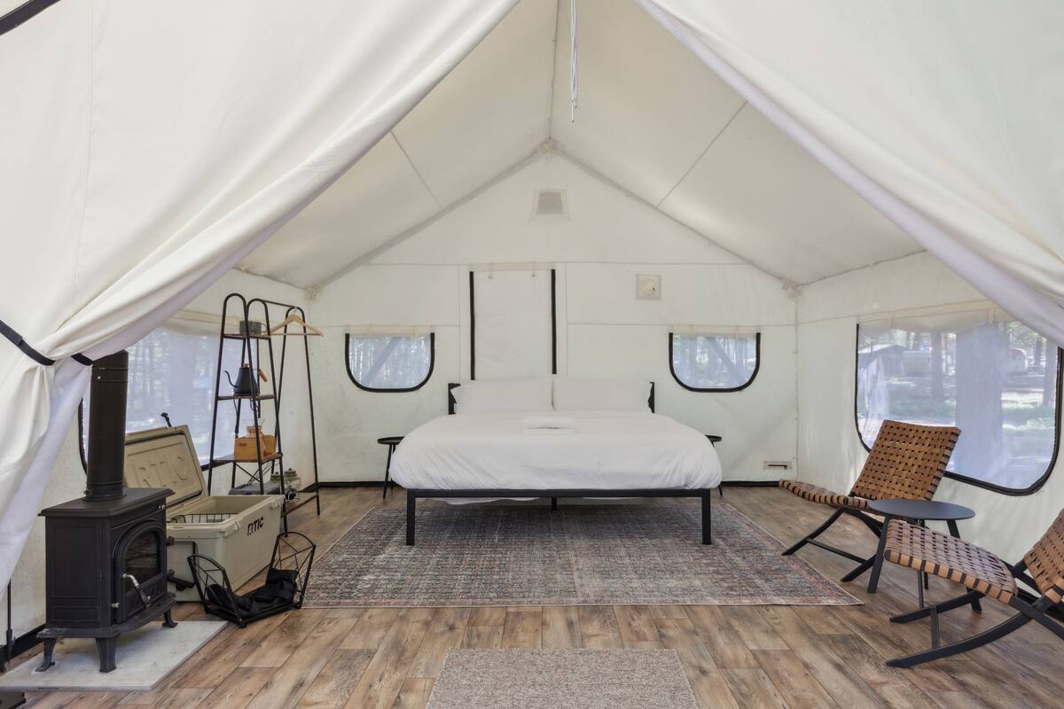A tent with a bed, a stove, and two rocking chairs.