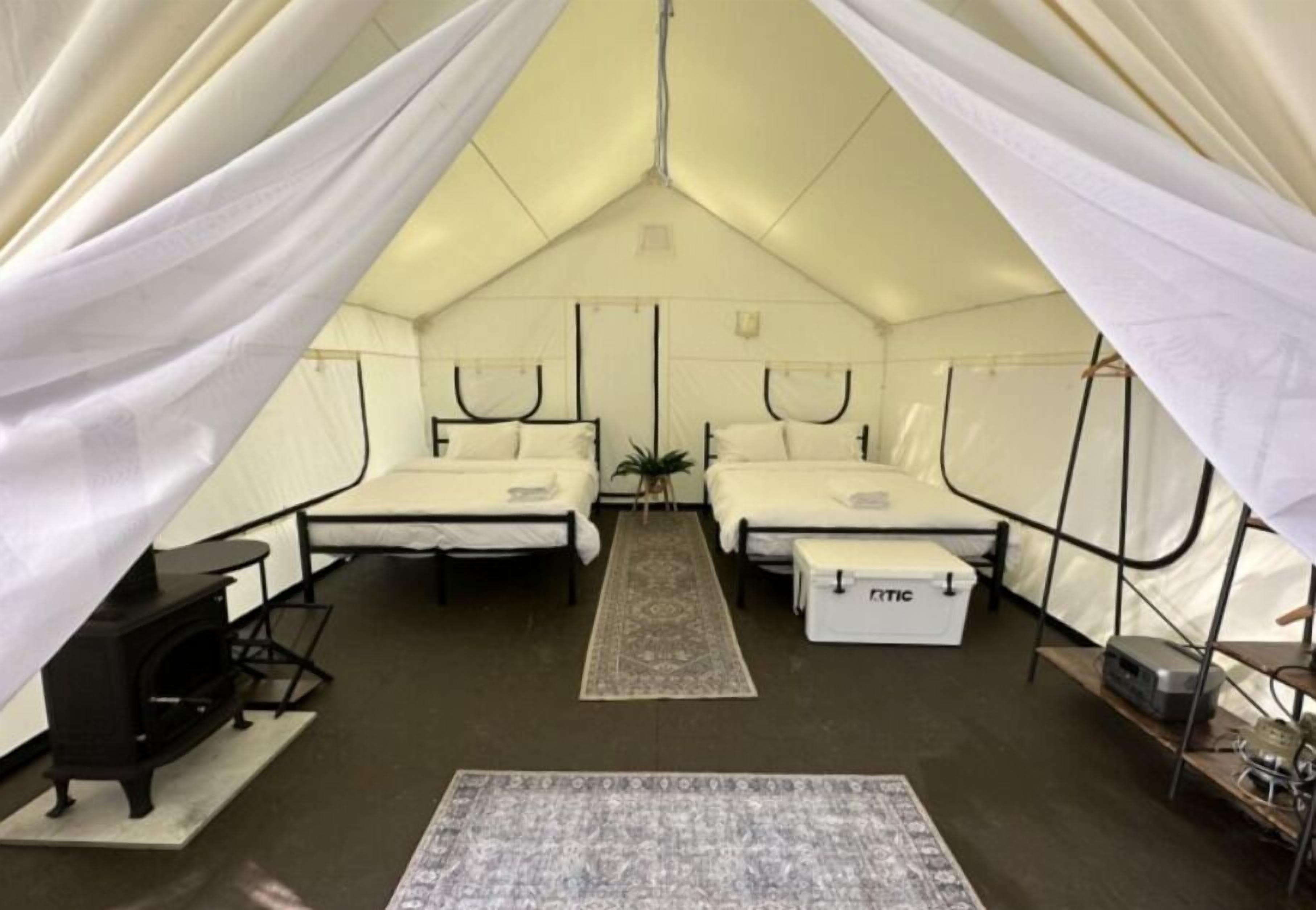 A tented accommodation with two beds, a small table, a bench, and a heater.