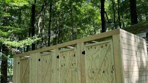A wooden cabin with a simple, rustic design, featuring a large door and windows, set in a forested area. - Ferncrest Campground (Greentown)