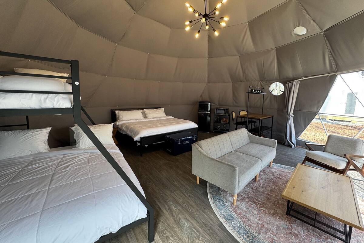 A tented accommodation with bunk beds, a sofa, a small table, a television, and a clock.