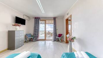 Habitación de hotel con dos camas, televisión, cómoda, silla y balcón con mesa y sillas.