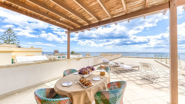 A covered outdoor dining area with a table set for two, chairs, and a view of the sea. - SUITE VISTA MARE (Santa Cesarea Terme)