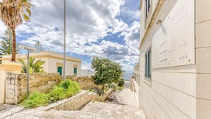 A narrow stone pathway leading to a building with a signboard advertising various brands. - SUITE VISTA MARE (Santa Cesarea Terme)