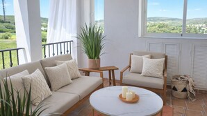 Ein Balkon mit Sofa, Sessel und Tisch, einer Topfpflanze und Blick ins Grüne.