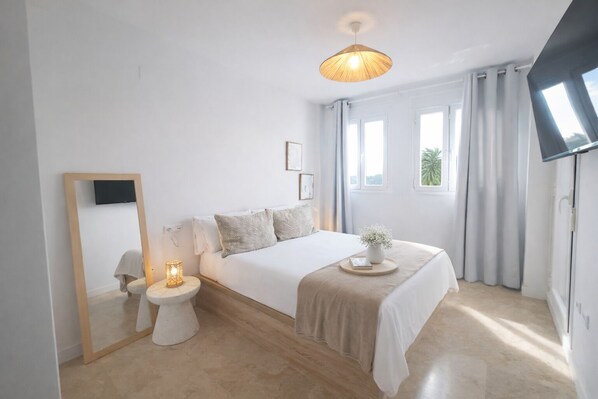 Une chambre à coucher moderne avec un grand lit, des tables de chevet, un miroir et un luminaire au plafond.