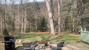 Une terrasse avec un barbecue, deux fauteuils Adirondack, une petite table et un mur en pierre.