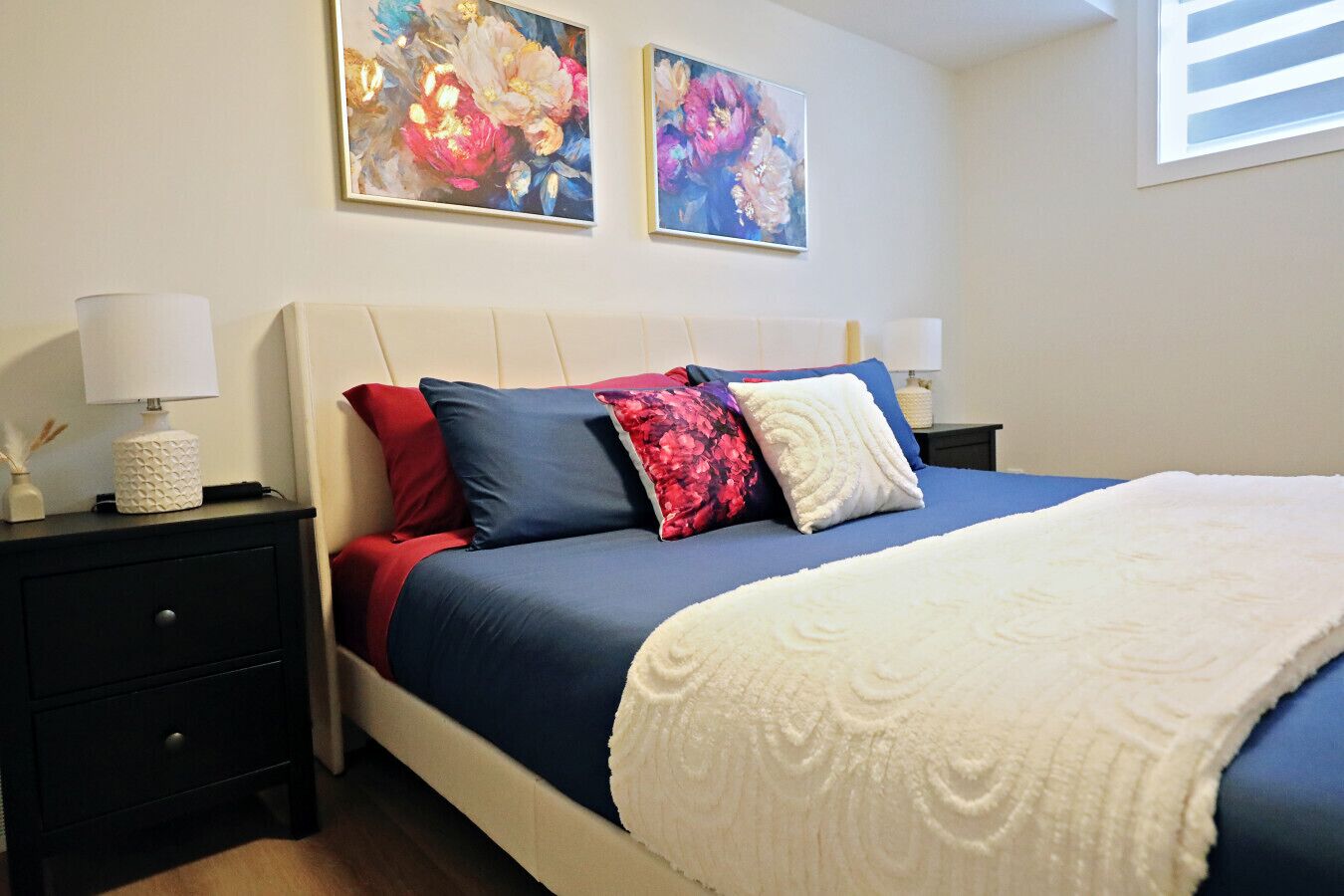 Une chambre à coucher avec un lit, deux tables de chevet, une lampe et deux tableaux au mur.