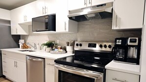 Una cocina moderna con armarios blancos, lavavajillas de acero inoxidable, estufa negra y cafetera.