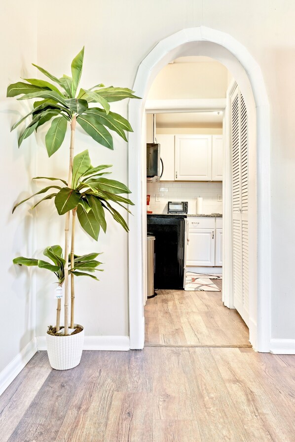 A hallway leading to a kitchen with white cabinets, a microwave, and a potted plant.