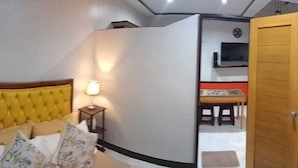 Quarto com cama, mesa de cabeceira, luminária e vista para uma sala de jantar.