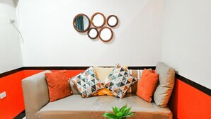 Uma sala de estar com um sofá, uma mesa de centro com uma planta e um espelho fixado na parede.