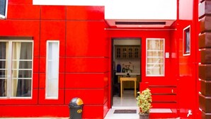 Um edifício vermelho com porta, janelas e um contentor de lixo.