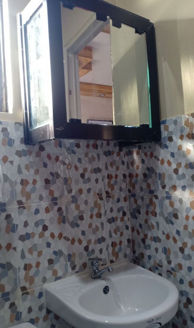Ein Badezimmer mit einem weißen Waschbecken, einem Spiegel und einer gefliesten Wand mit geometrischem Muster.