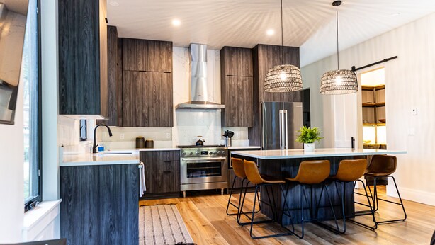 A modern kitchen with dark wood cabinets, stainless steel appliances, and a central island with bar stools. - New Luxury Home in the Heart of Ouray, Walk Main St, Breathtaking Views, AC (Ouray)