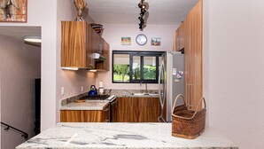 A compact kitchen with wooden cabinets, a marble countertop, a built-in stove, and a window with a view of greenery.