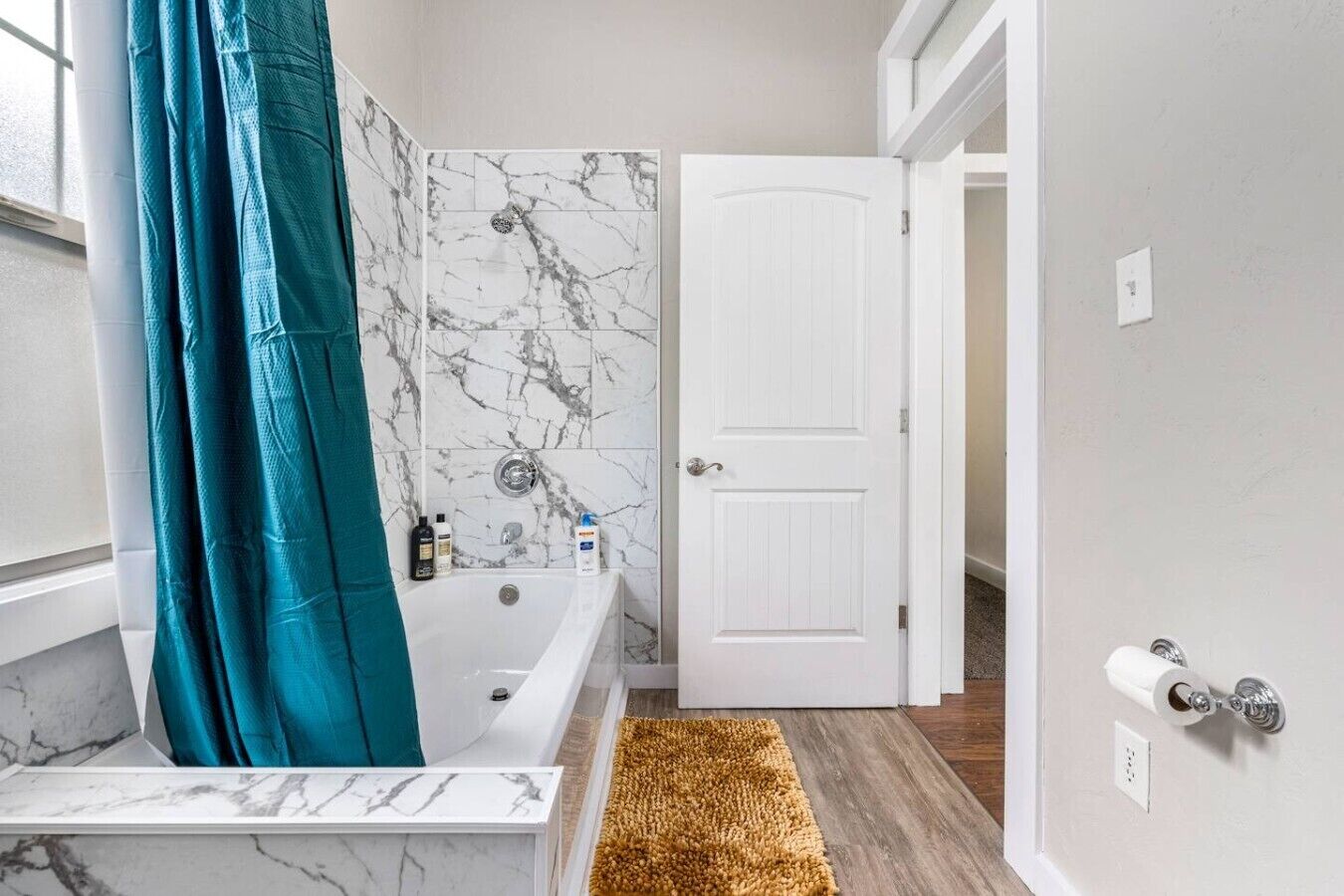 A bathroom with a bathtub, a white door, and a marble wall.