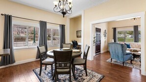 A dining area with a round table, chairs, and a chandelier. There is a view through the window, and a living room with a sofa and a chair is visible. - Quiet Home Near Downtown + Mountain Views (Salt Lake City)