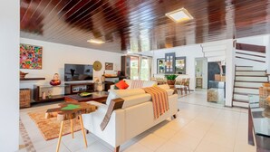 Amplia sala de estar con un sofá blanco, una mesa de centro de madera y una escalera que lleva a otro nivel.