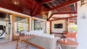 Un área exterior moderna para disfrutar, con un sofá de mimbre, una mesa redonda y una pared de piedra con un televisor de pantalla plana.