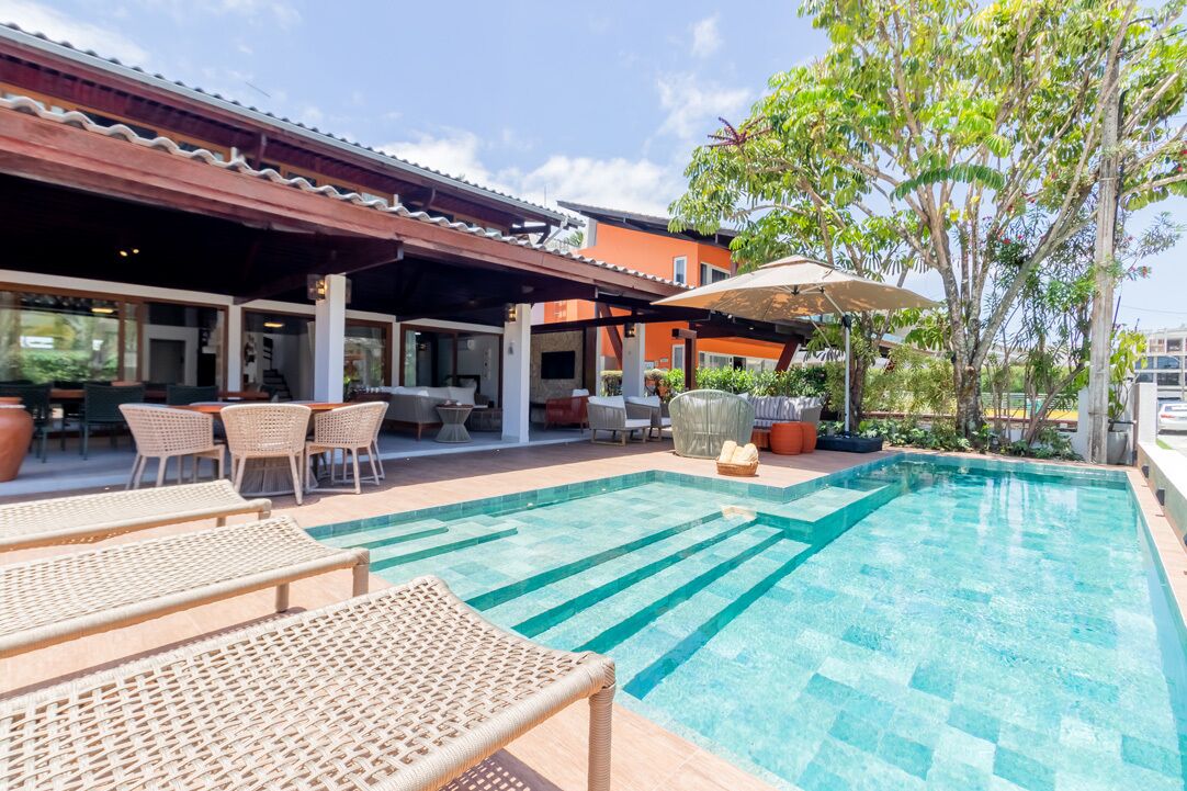 A pool area with lounge chairs, a covered seating area, and a building with a tiled roof.