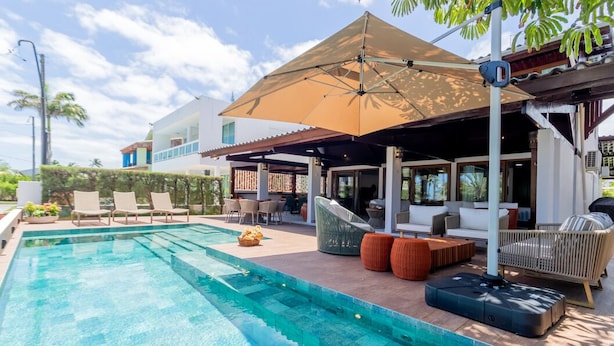 Piscina con sillones de descanso y una zona de estar techada.