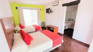 Ein Hotelzimmer mit zwei Betten, einem Schreibtisch, einem Stuhl, einem Fenster mit Vorhängen, einer Klimaanlage und einem durchgehenden Badezimmer.