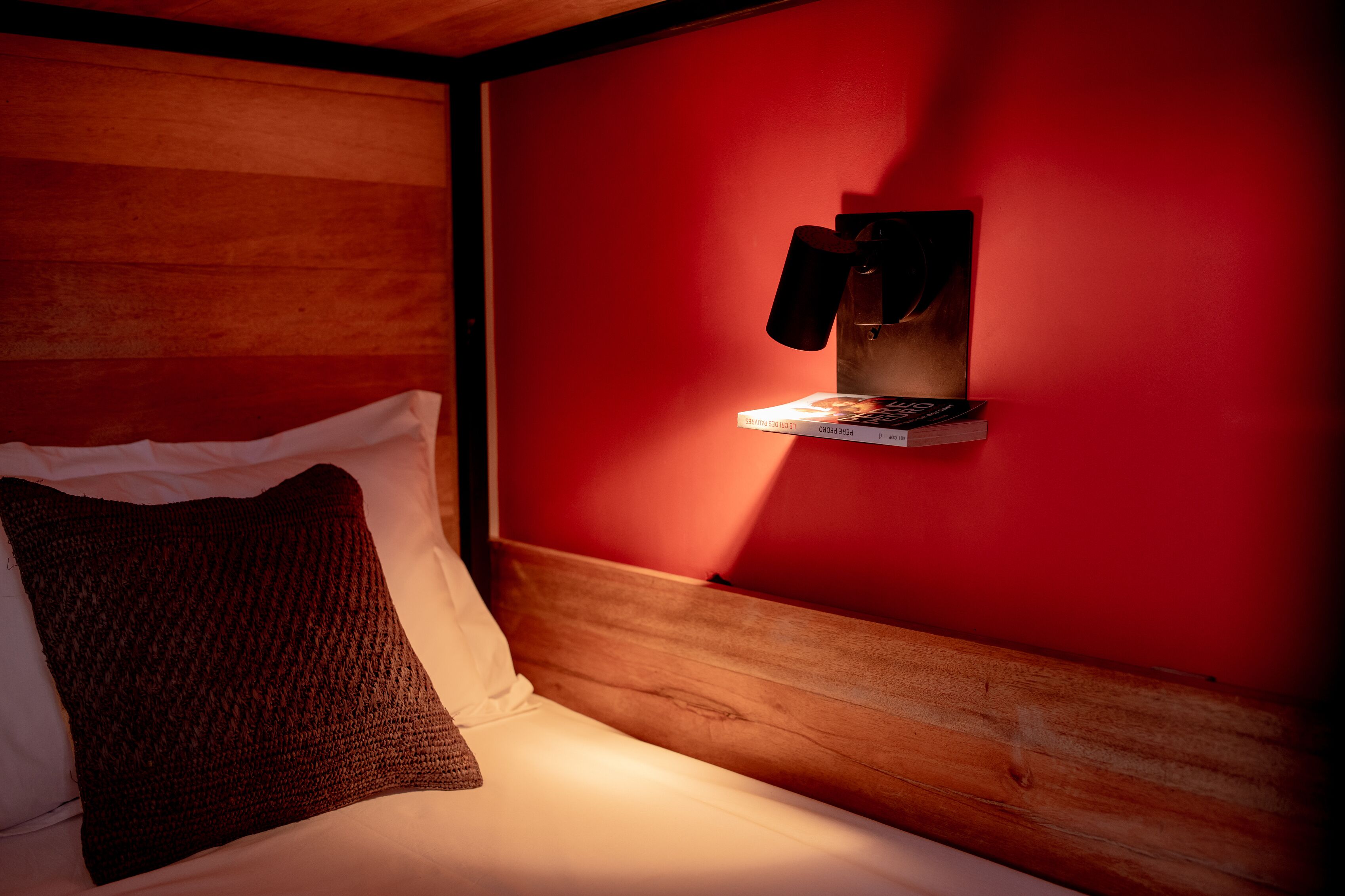 A cozy room with a wooden headboard, a red wall, and a shelf with a book and a phone.