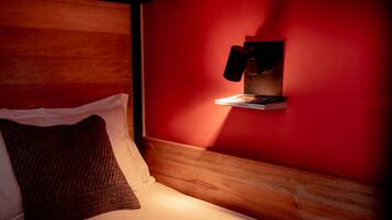 A cozy room with a wooden headboard, a red wall, and a shelf with a book and a phone.