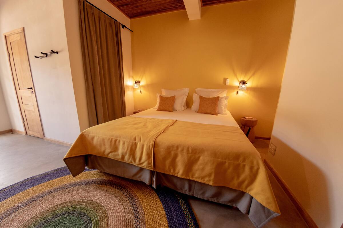A hotel room with a bed, two bedside lamps, a wooden door, and a patterned rug.