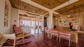 Una habitación amplia con suelo de madera, un área de comedor con sillas rosas, una zona de bar con un mural colorido y un ventanal que deja entrar luz natural.