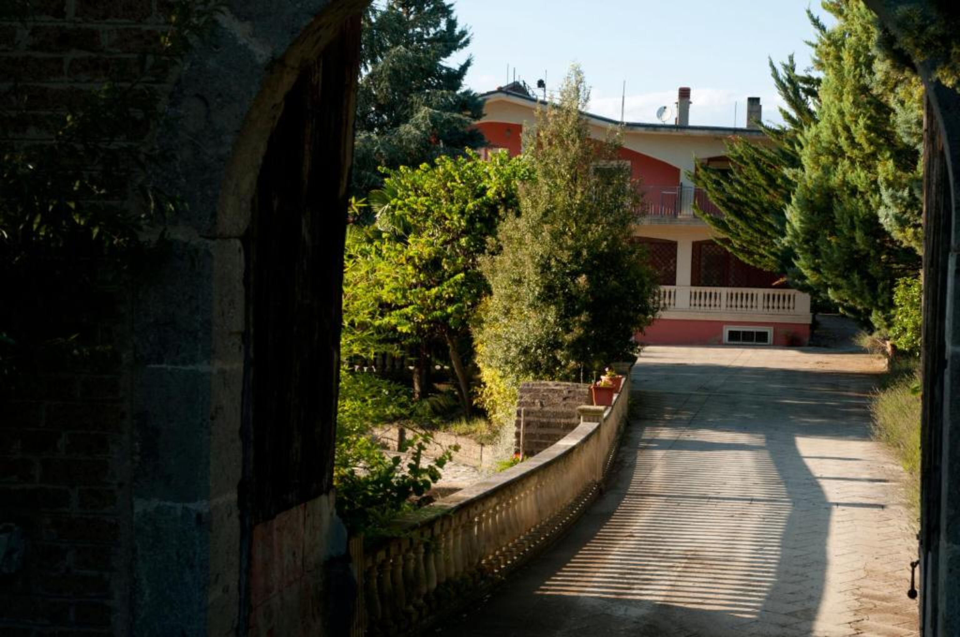 A narrow pathway leading to a building with a red facade and a balcony.