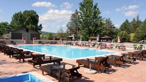 Zona de piscina con sillones de madera y un edificio pequeño al fondo.