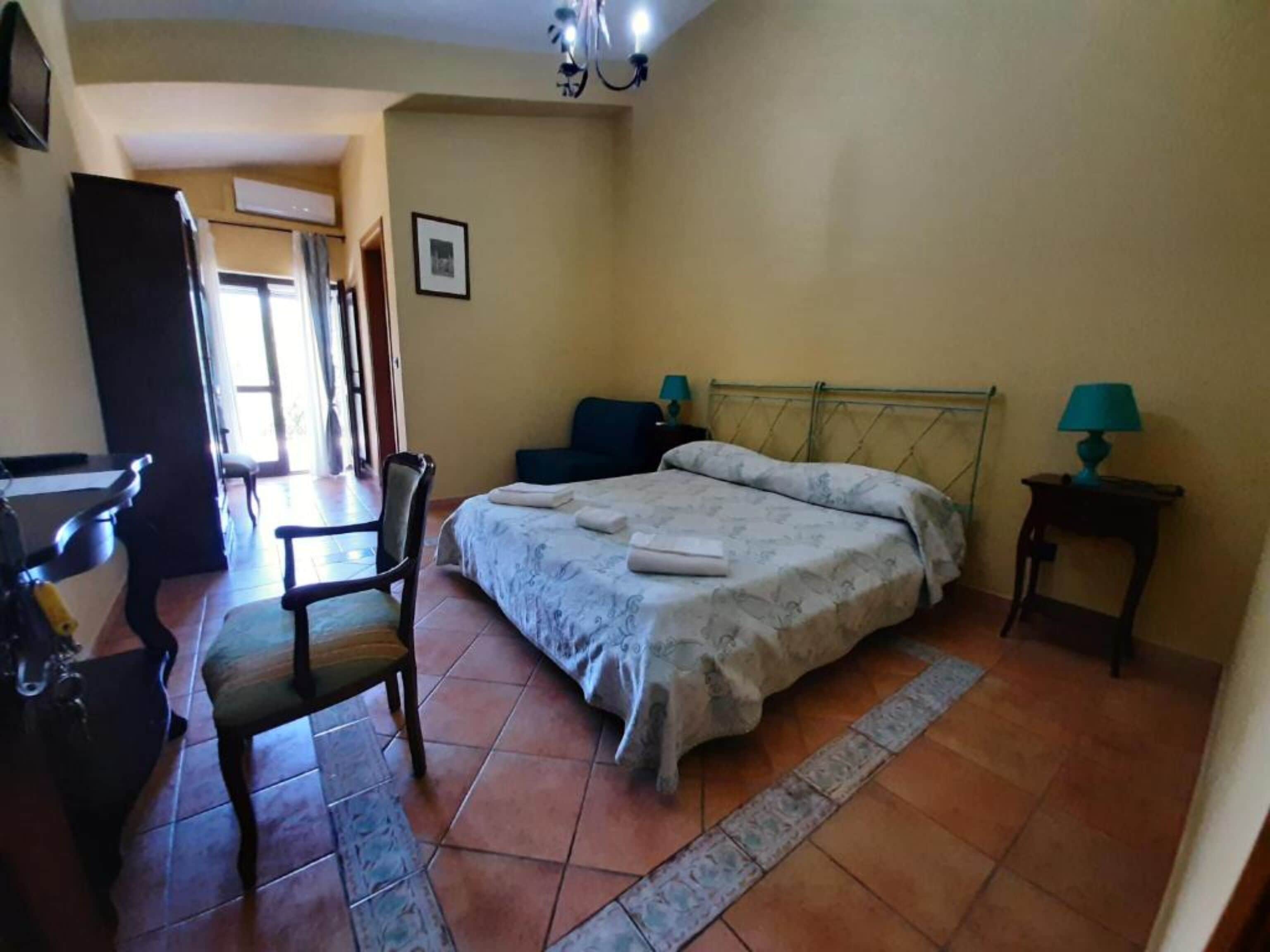 A bedroom with a bed, a chair, a desk, and a lamp.