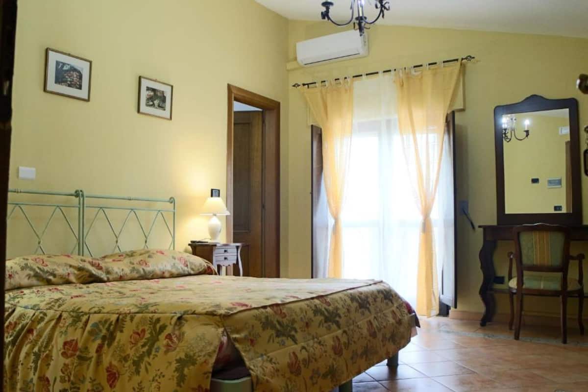 A bedroom with a bed, a nightstand, a chair, a mirror, and a door.