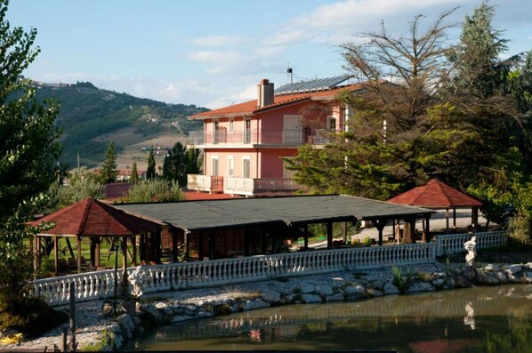 A two-story building with a balcony, a covered outdoor area with a fence, and a body of water in the foreground.