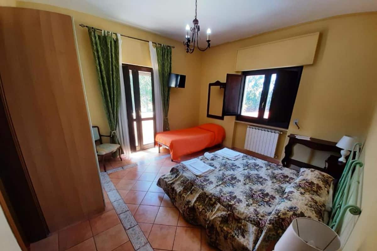 A bedroom with a bed, a chair, a TV, a radiator, and a window.