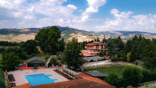 Un hotel con piscina, un edificio grande de techo rojo y vistas de las colinas circundantes.
