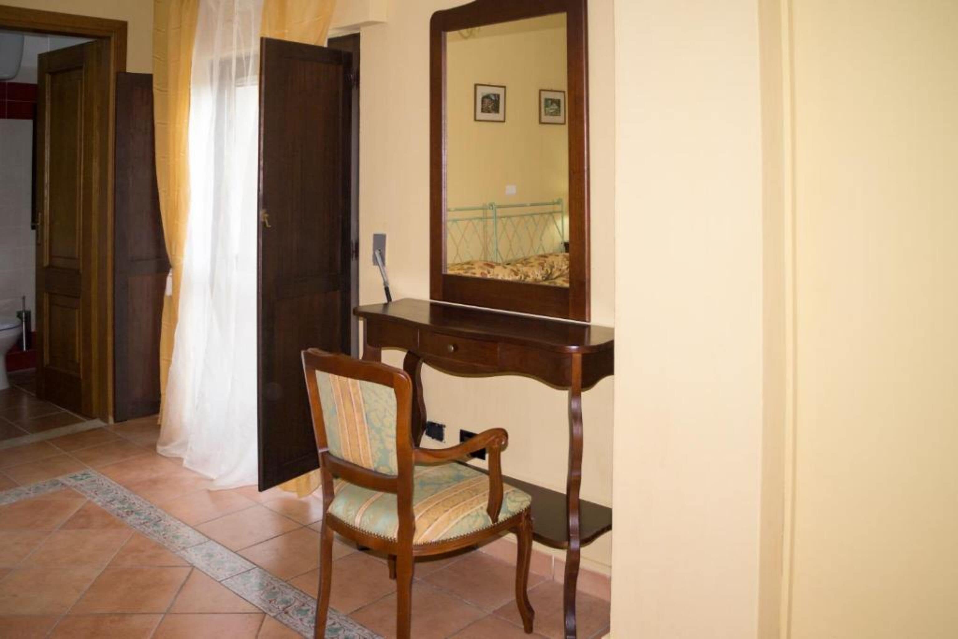 Una habitación con escritorio de madera, una silla, un espejo y una puerta.