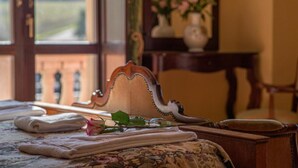 Una cama bien hecha con toallas dobladas y una rosa sobre el edredón, una silla de madera y un jarrón con flores sobre una mesa.