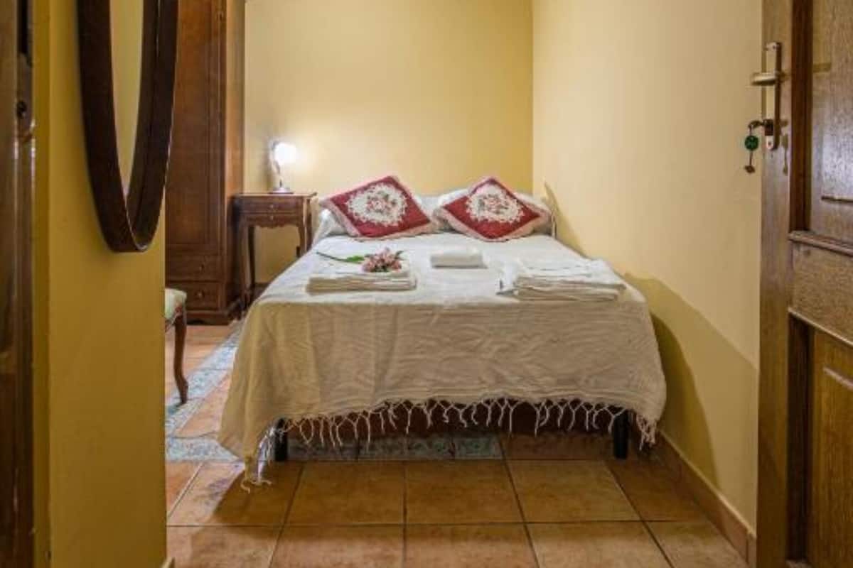 A narrow hallway leading to a bedroom with a bed, a mirror, and an air conditioning unit on the wall.