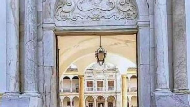 Un ingresso maestoso caratterizzato da colonne elaborate e un arco decorato, che conduce a un cortile con un edificio sullo sfondo.