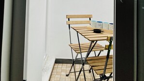 Un corridoio stretto che conduce a una zona pranzo con tavolo e sedie, una pianta in vaso, un lampadario a parete e una finestra.