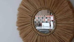 Uno specchio rotondo con cornice in legno che riflette una stanza con parete bianca, una lavagna e una stampante.