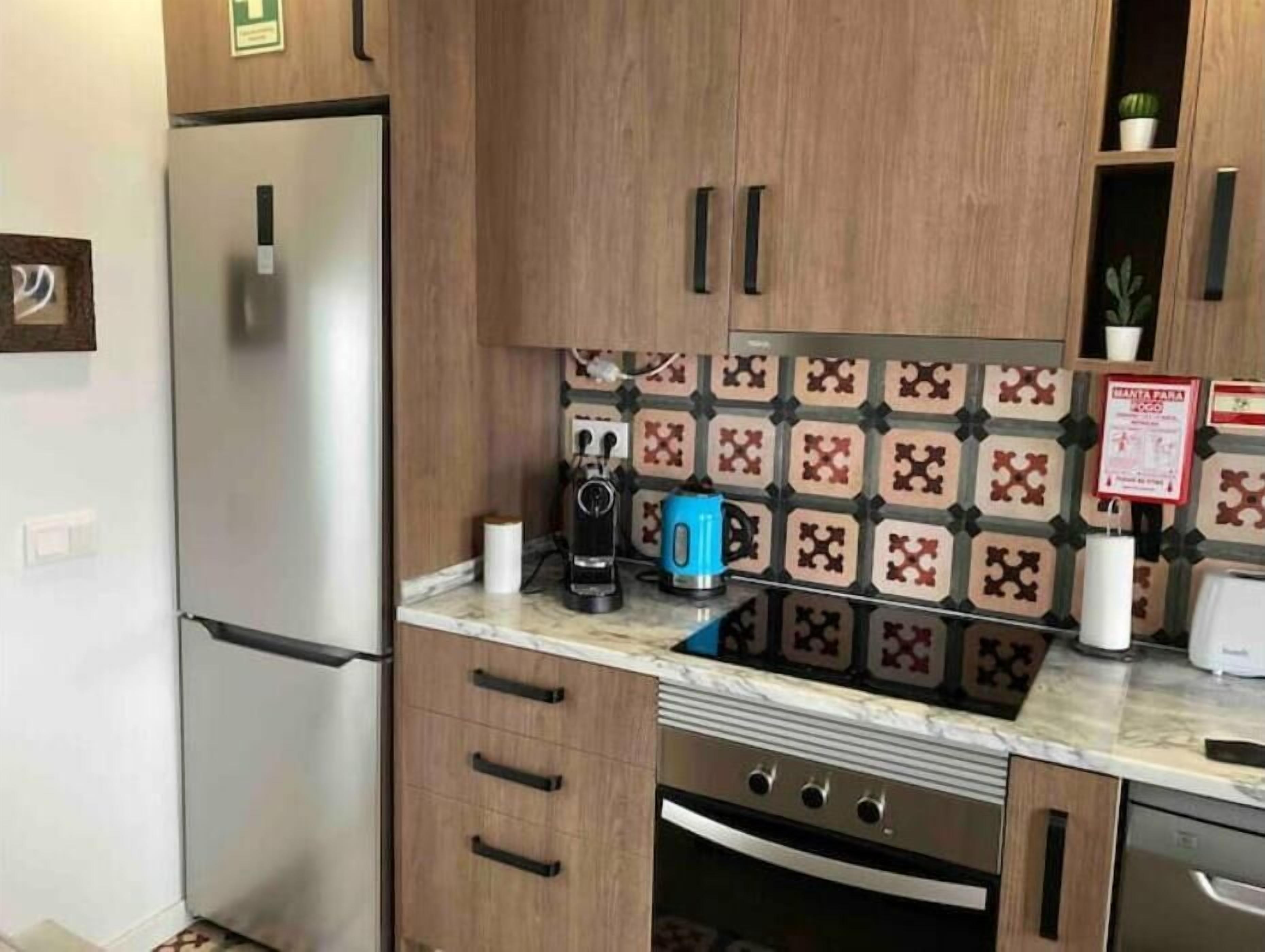 Eine Küche mit Holzausstattung, einem Edelstahlkühlschrank, einer Kaffeemaschine und einer gefliesten Spritzschutzwand.