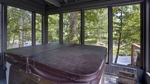 A room with a large window overlooking a forested area, a wooden bench, and a wicker basket. - Sunny Creekside Getaway (Cosby)