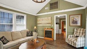 A living room with a sofa, armchair, and fireplace. There is a painting on the wall and a door leading to another room. - Sunny Creekside Getaway (Cosby)
