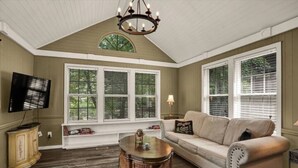 A living room with a beige sofa, a round coffee table, and a television on a wooden cabinet. - Sunny Creekside Getaway (Cosby)