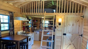 A cozy cabin interior with a kitchen, dining area, and a loft bedroom. - Secluded Off-Grid Cabin, Upper Peninsula Getaway on 36 Private Acres (Bruce Crossing)