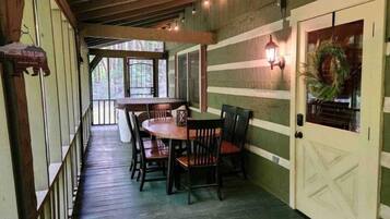 A wooden deck with a table and chairs, a door with a wreath, and a sign that reads "Welcome to Cabin."